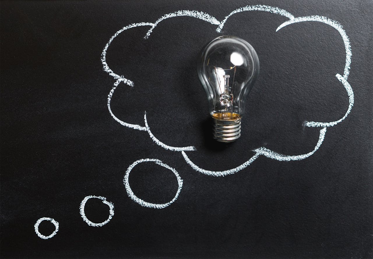 About Light bulb laying on chalkboard with drawn thought bubble, symbolizing creative ideas.
